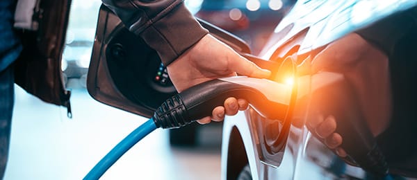 Human hand is holding Electric Car Charging connect to Electric car